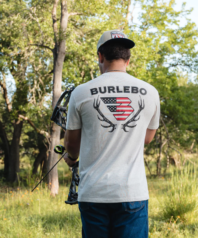 Man wearing a 'Burlebo' t-shirt with an American flag design in a forest setting