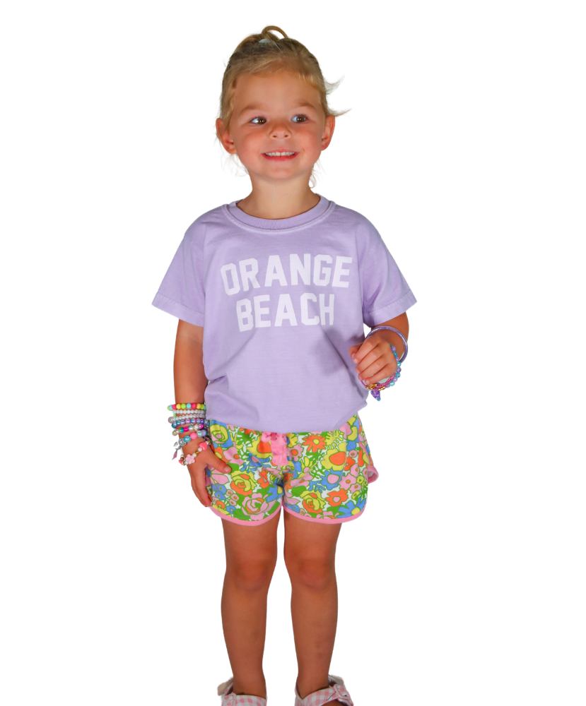 Child wearing a purple 'Orange Beach' shirt and colorful shorts on a white background