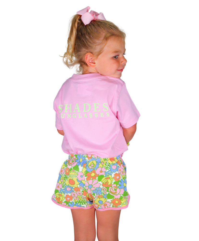 Child wearing a pink shirt with 'Shades of Pink' text and colorful floral shorts on a white background