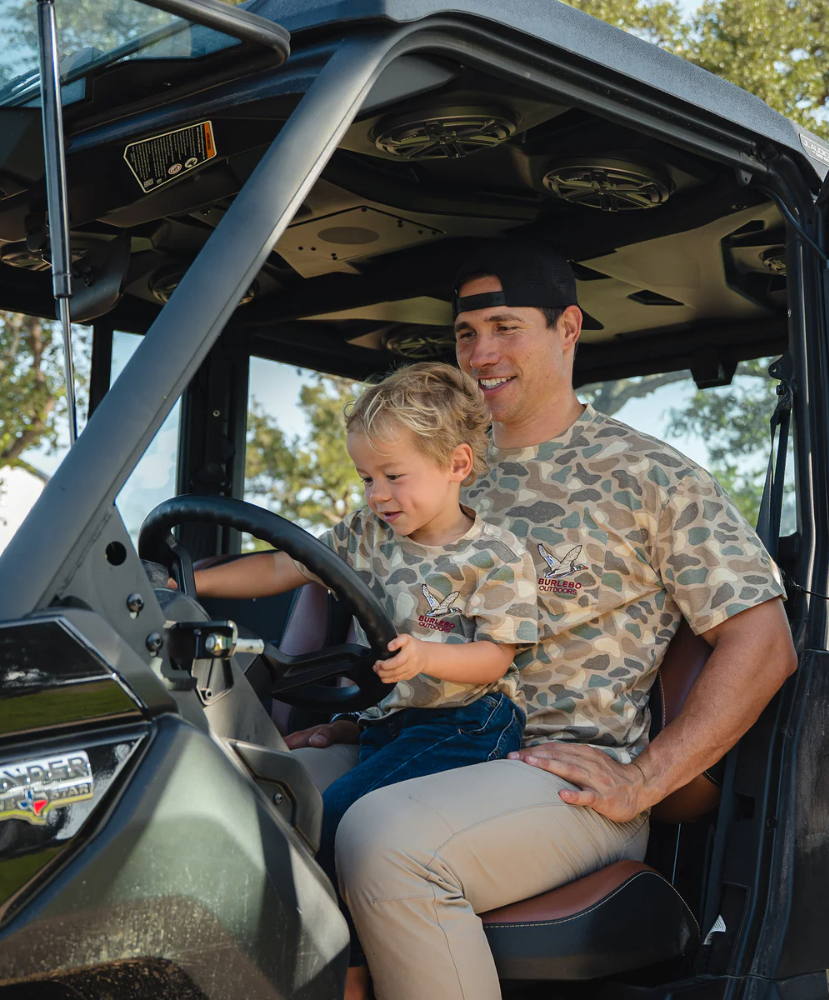 Man and child sitting inside a vehicle with trees in the background