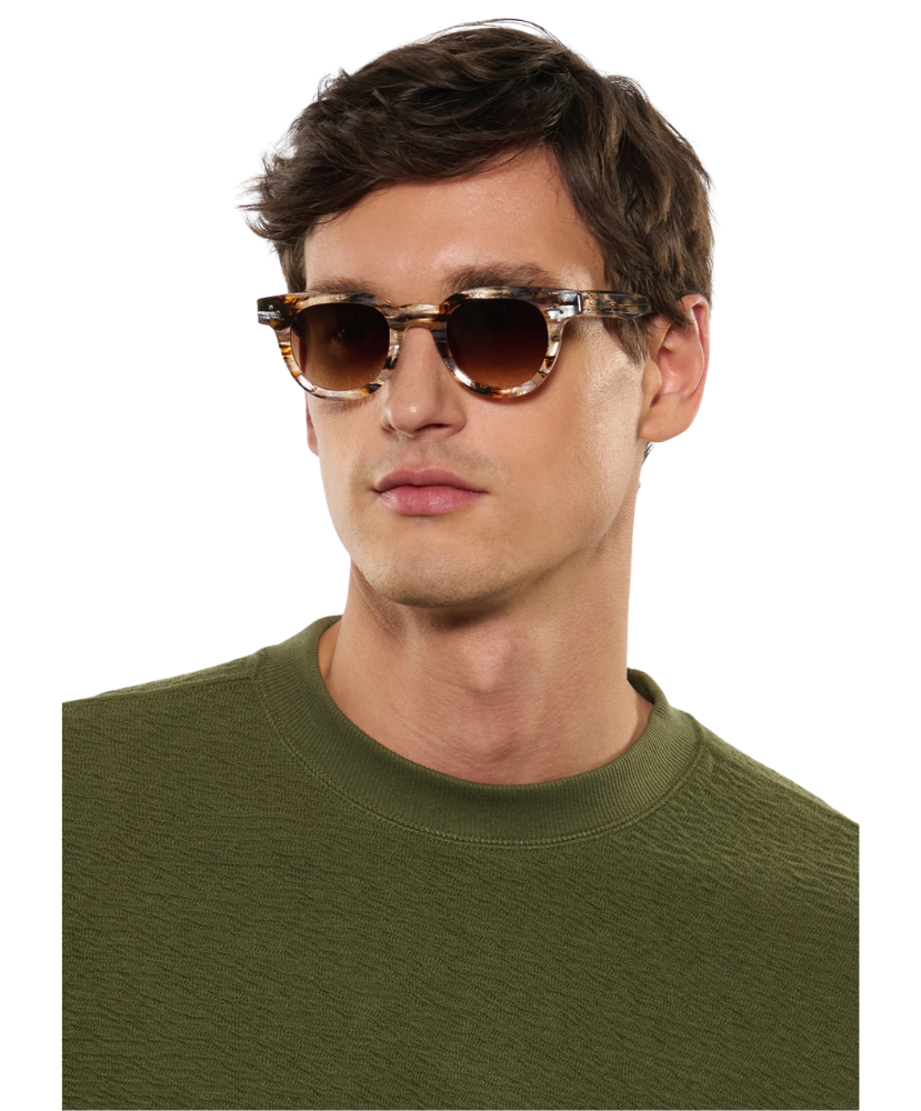 Man wearing Krewe sunglasses and a green sweater on a white background