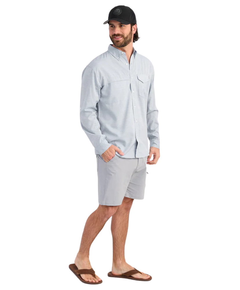 Man wearing a light blue performance HUK button-up shirt and black cap on a white background