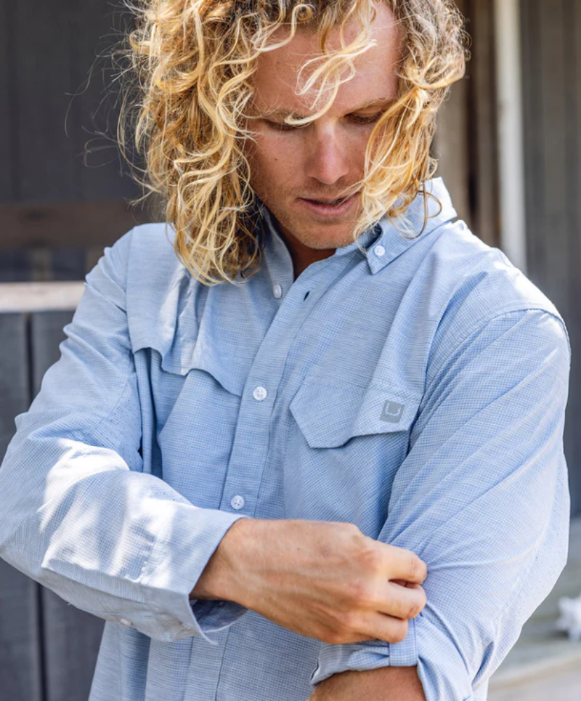 Man wearing a light blue Button up Huk shirt with rolled-up sleeves, standing outdoors.