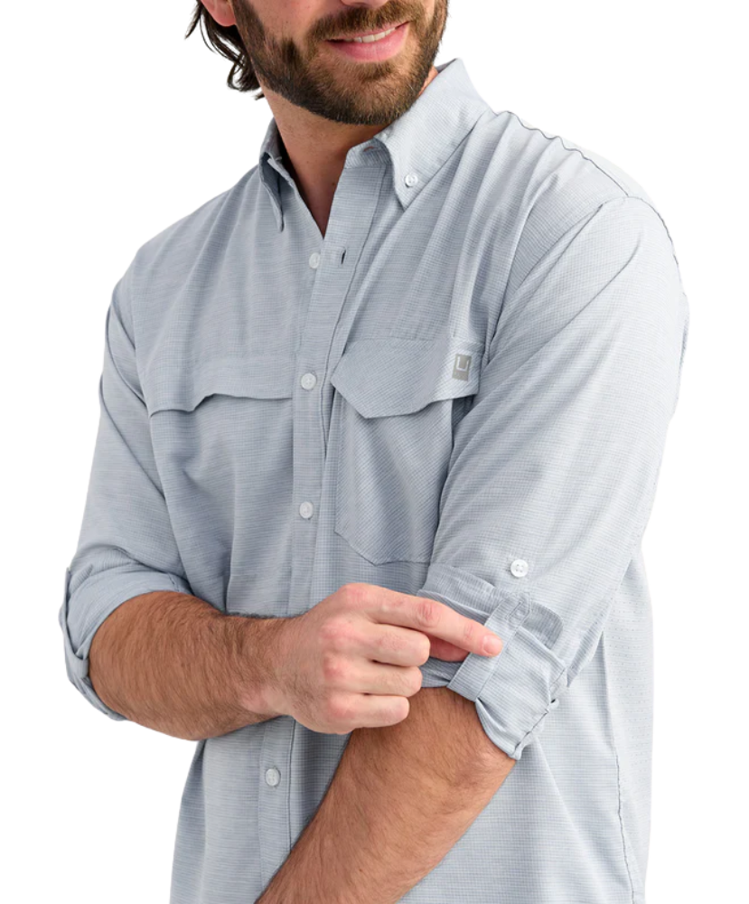 Man wearing a light blue performance HUK button-up shirt and black cap on a white background