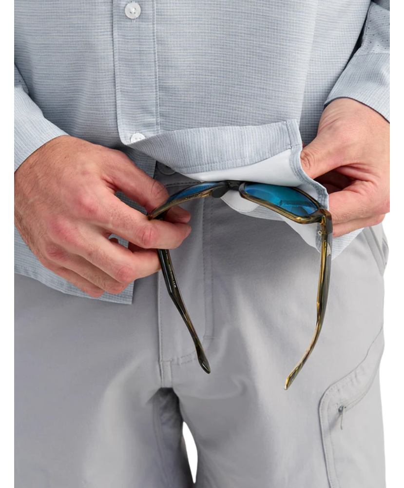 Person wearing a light gray huk button up shirt and pants, cleaning sunglasses with interior glass wipe sunglasses with a white background