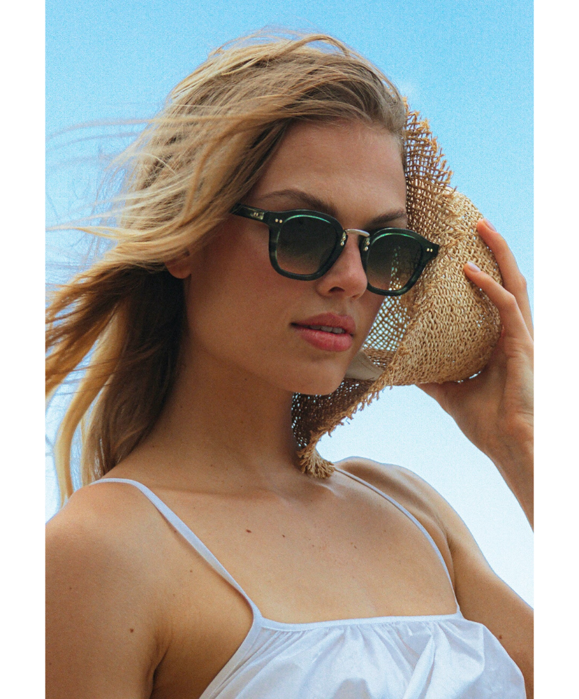 Woman wearing krewe sunglasses and a straw hat against a clear blue sky