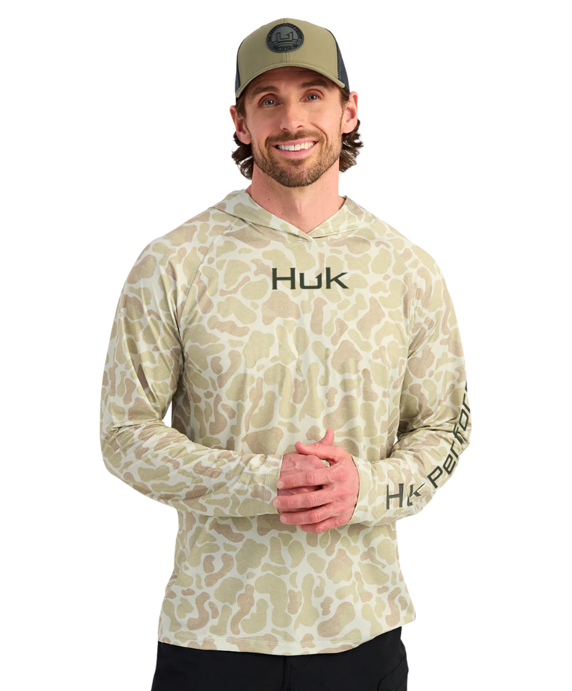 Man wearing a sand camouflage hoodie with 'Huk' branding on a white background