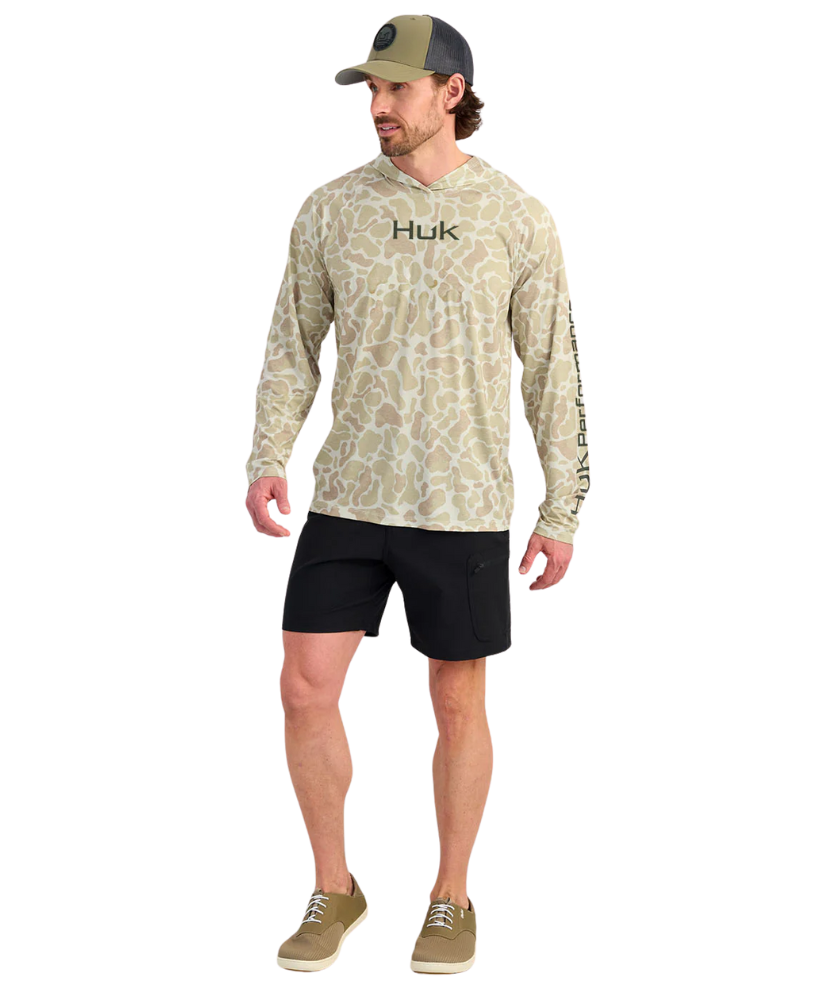 Man wearing a sand camouflage hoodie with 'Huk' branding on a white background