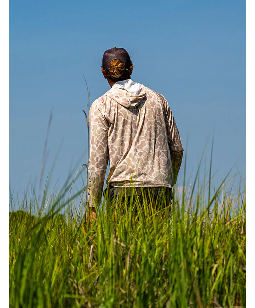 Man wearing a sand camouflage hoodie with 'Huk' branding on a white background