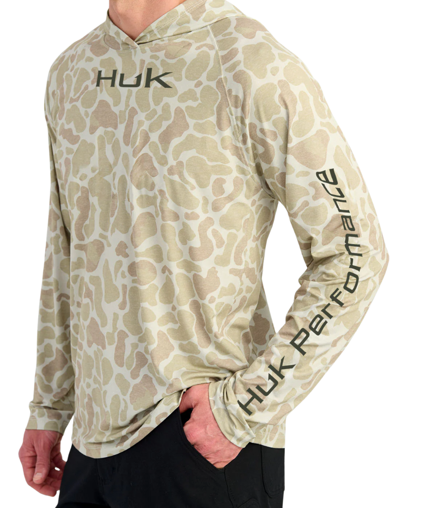 Man wearing a sand camouflage hoodie with 'Huk' branding on a white background