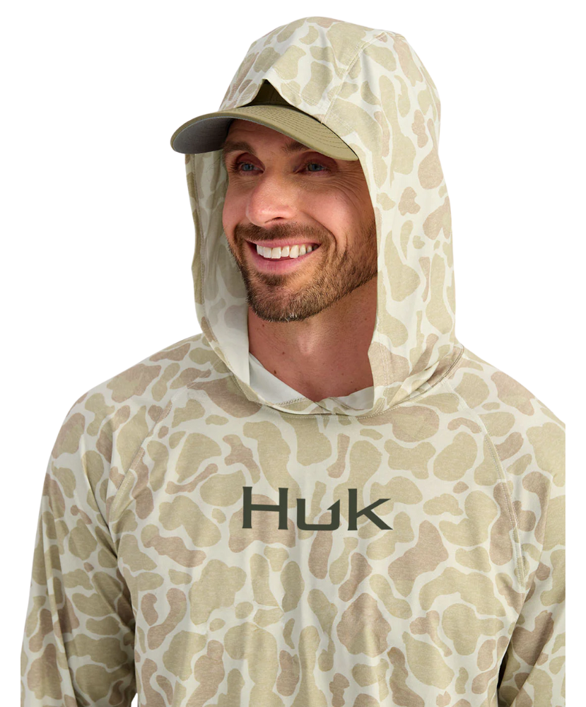 Man wearing a sand camouflage hoodie with 'Huk' branding on a white background