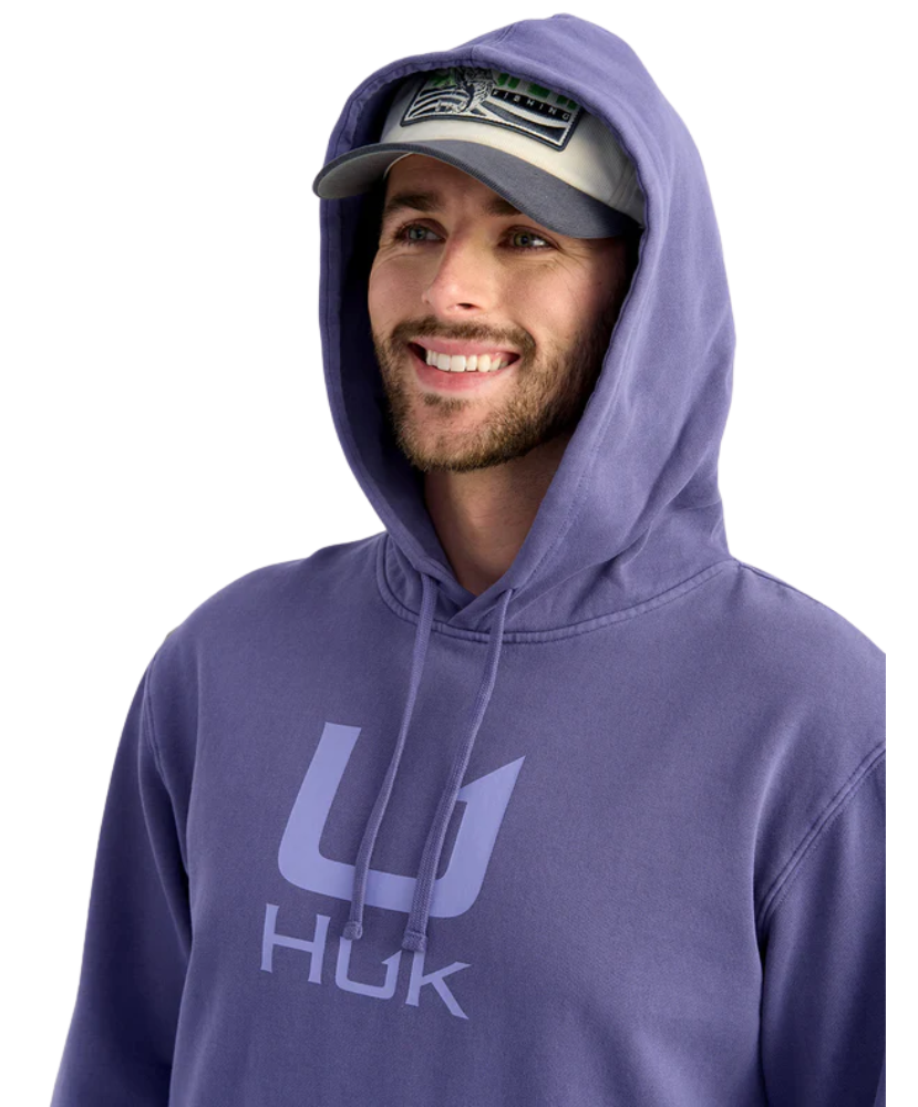Man wearing a purple hoodie with 'HUK' logo and a cap on a white background