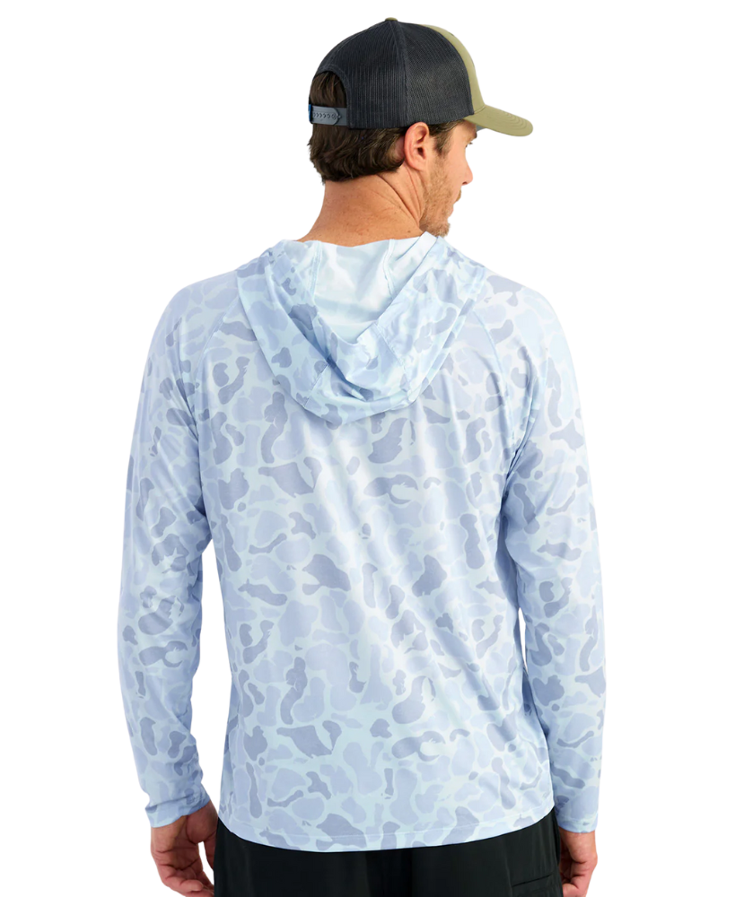 Man wearing a light blue camouflage hoodie with 'Huk' logo and a green cap on a white background