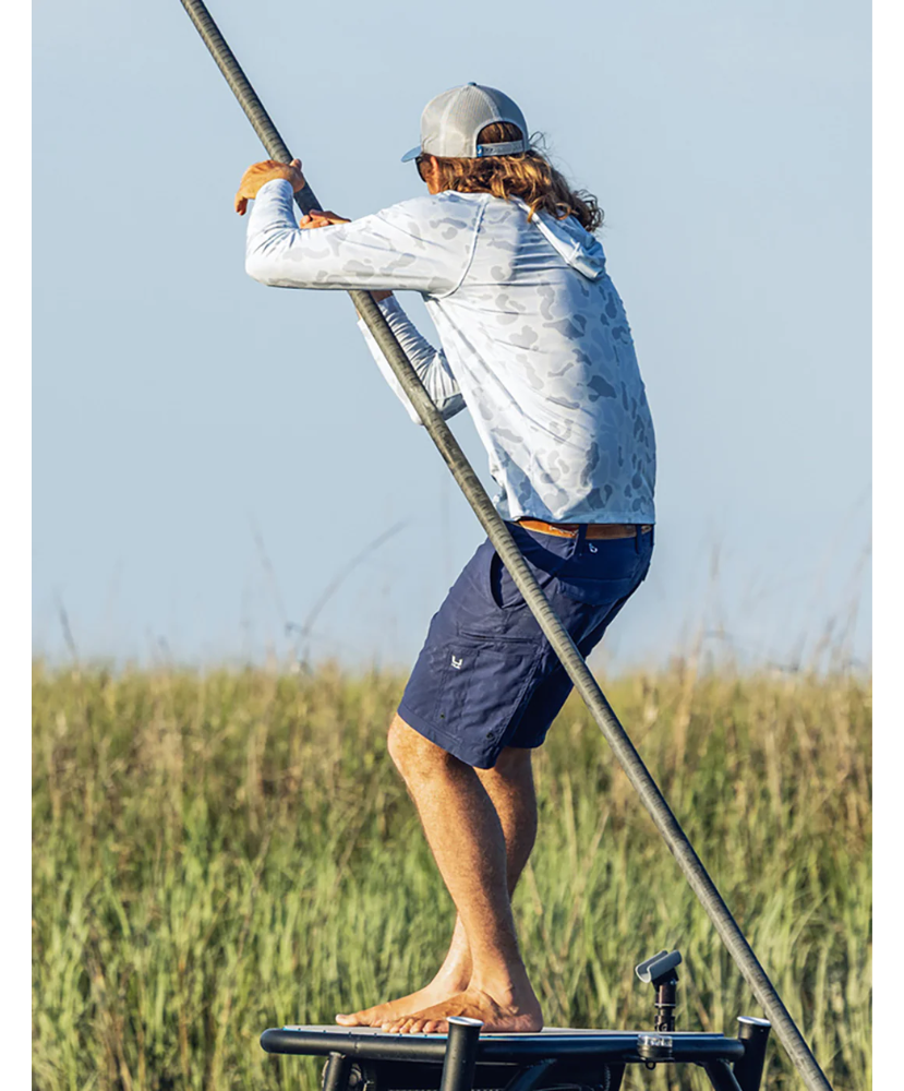 Man wearing a light blue camouflage hoodie with 'Huk' logo and a green cap on a white background