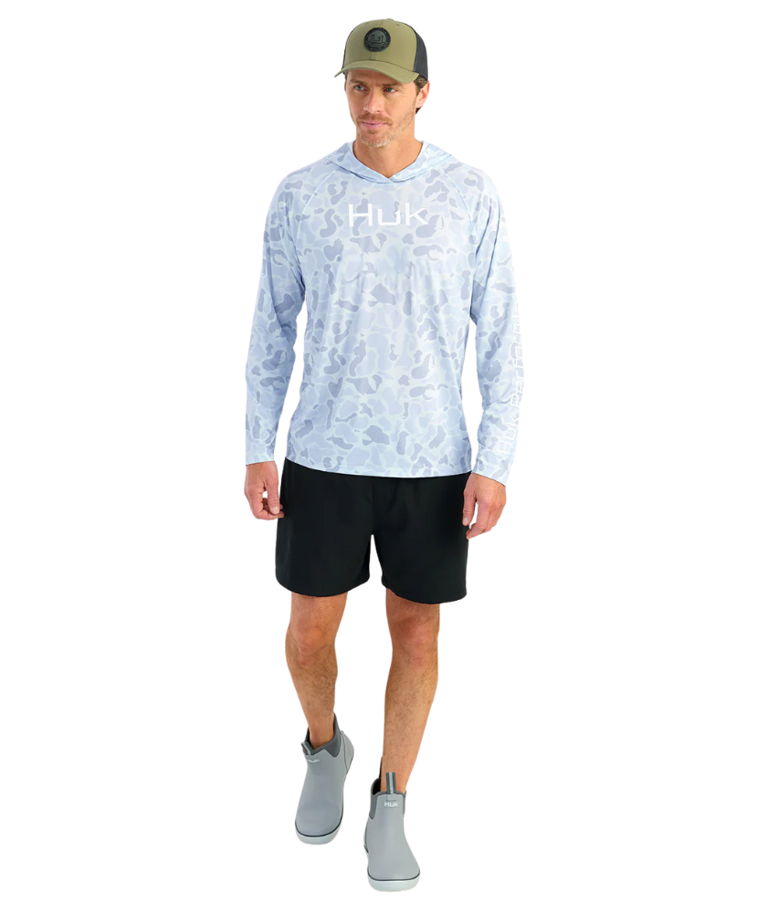 Man wearing a light blue camouflage hoodie with 'Huk' logo and a green cap on a white background