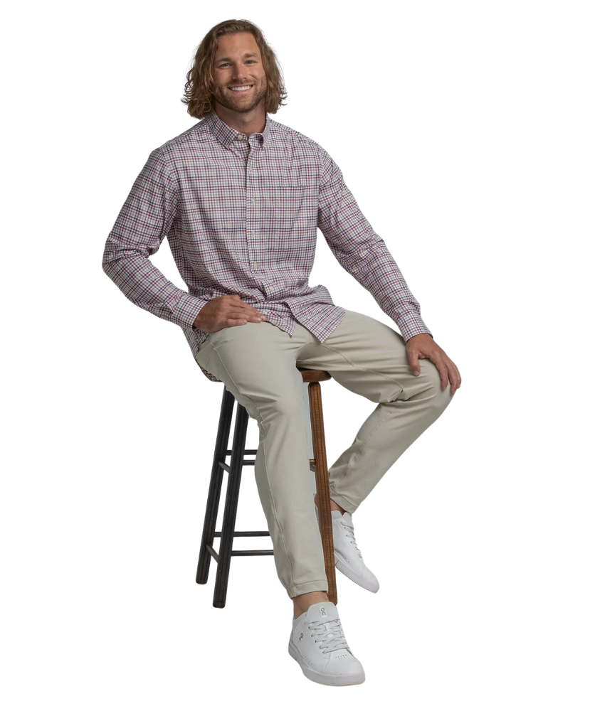 Man sitting on a stool wearing a checkered shirt and beige pants against a white background