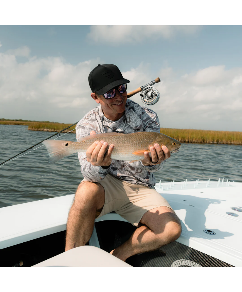 Man holding a fish on a boat with a fishing rod, surrounded by water and sky.