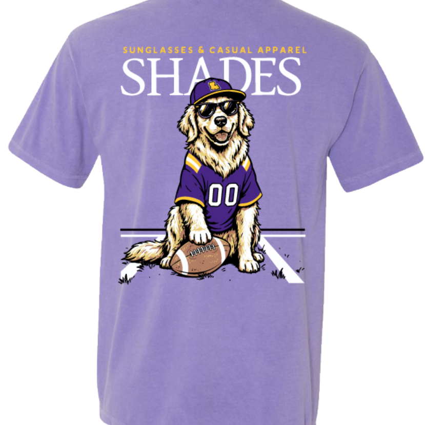 A purple short-sleeve t-shirt with a large graphic on the back. The graphic features the text 'SUNGLASSES & GUNGLASSES APPAREL SHADES' in white and yellow, with a cartoon golden retriever wearing a purple and gold football jersey and a matching cap, sitting on a football.