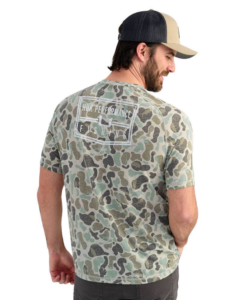 Man wearing a camouflage t-shirt with 'HUK Performance' logo on the back, standing against a white background.