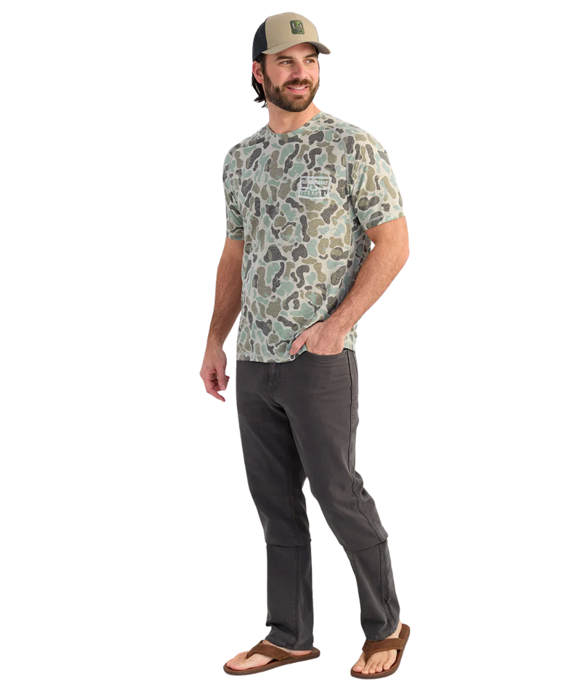 Man wearing a camouflage t-shirt and dark pants on a white background