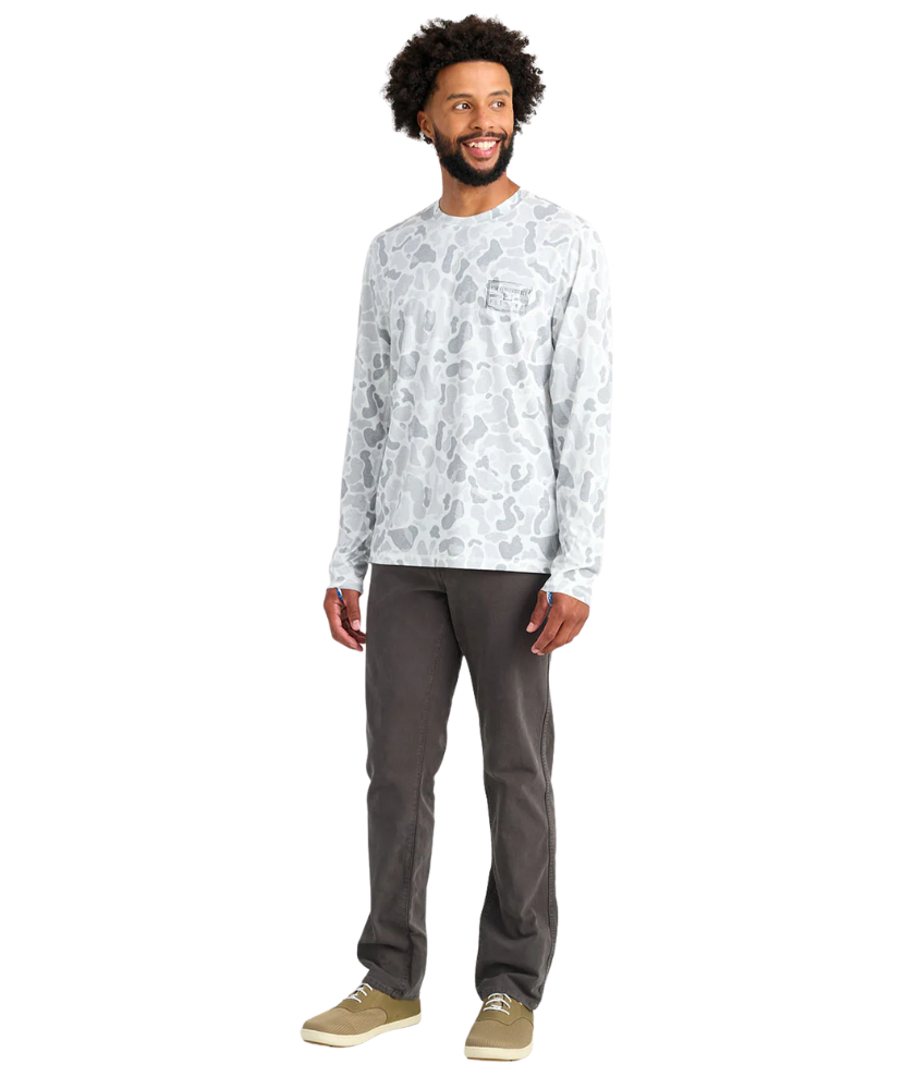 Man wearing a white long-sleeve shirt with a white camoflage pattern and dark pants on a white background