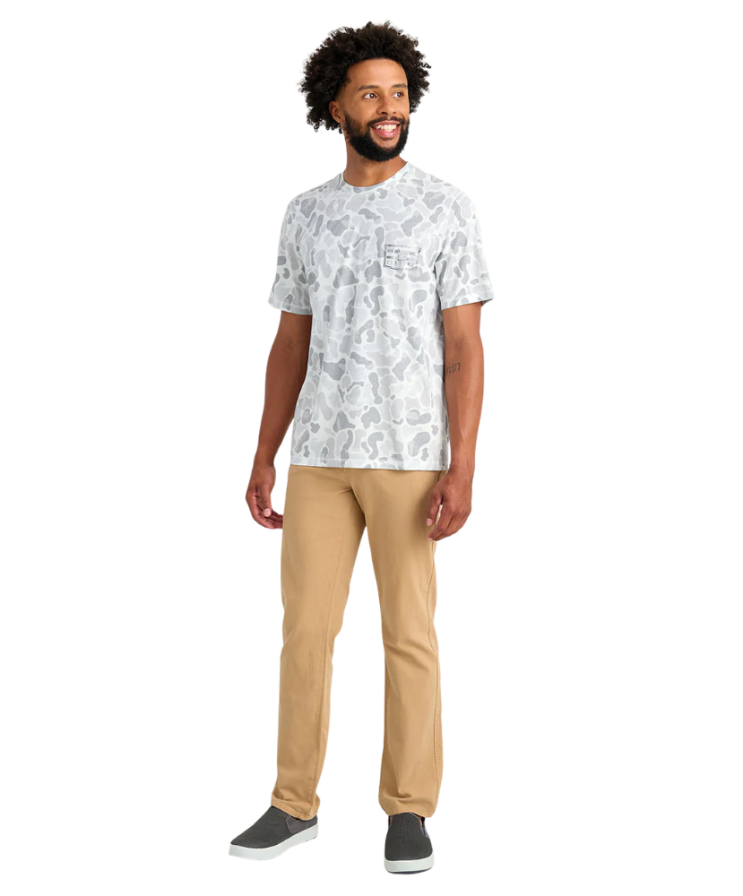 Man wearing a white patterned t-shirt and beige pants on a white background