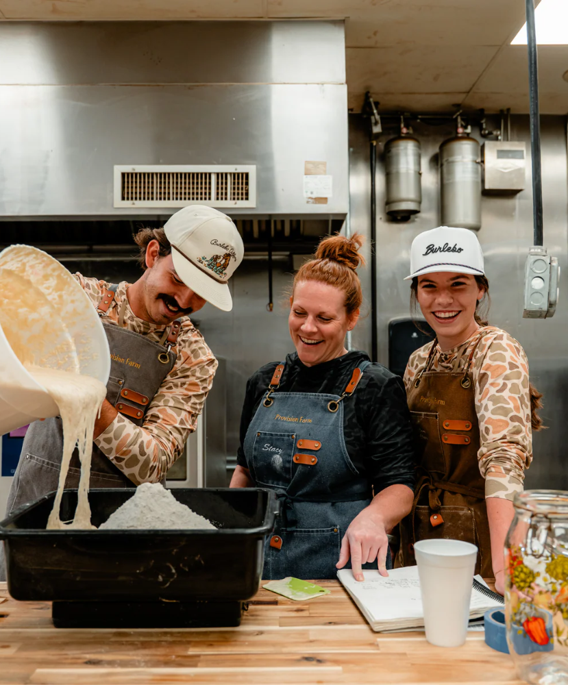 Three people in a kitchen, with one person pouring a liquid into a bowl.