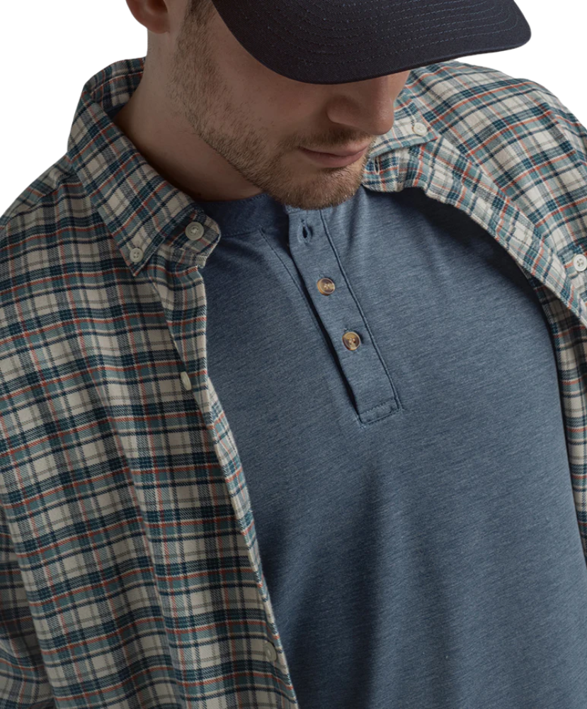 Man wearing a blue plaid shirt over a blue henley shirt with a neutral background