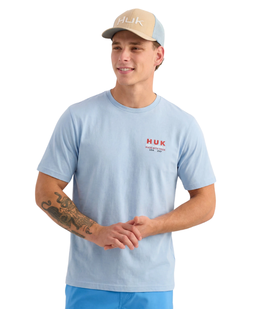 Man wearing a light blue HUK shirt and beige cap on a white background