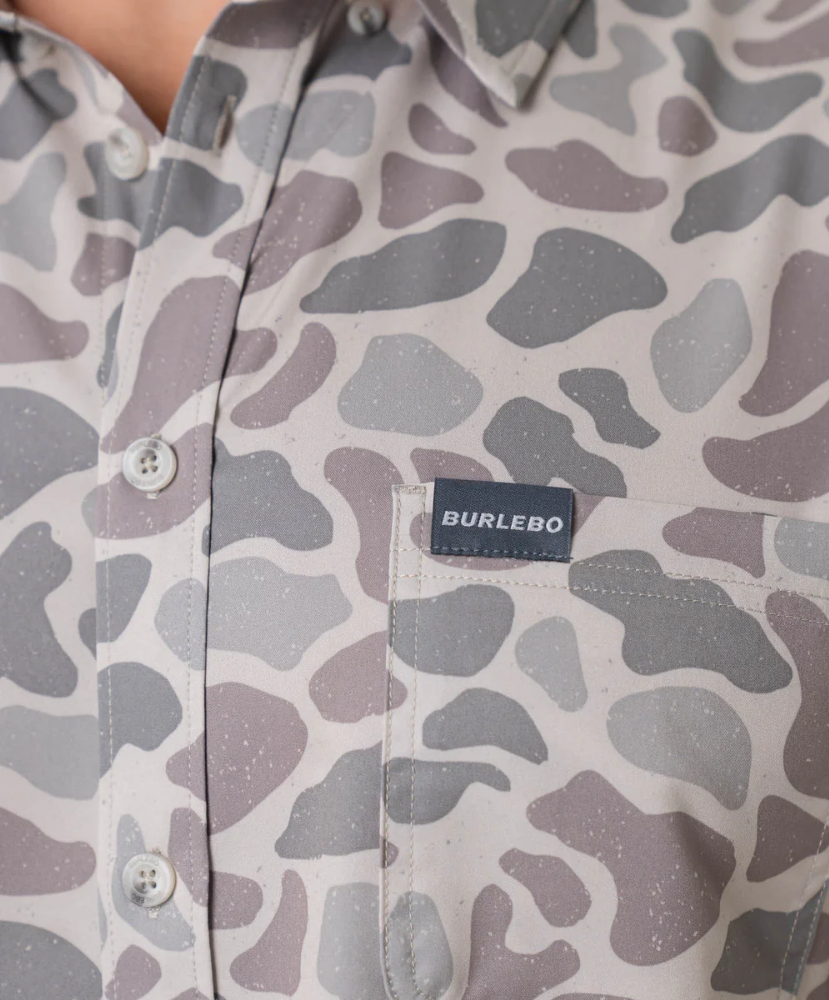 Person wearing a camouflage-patterned button-down shirt with a visible brand logo on a white background