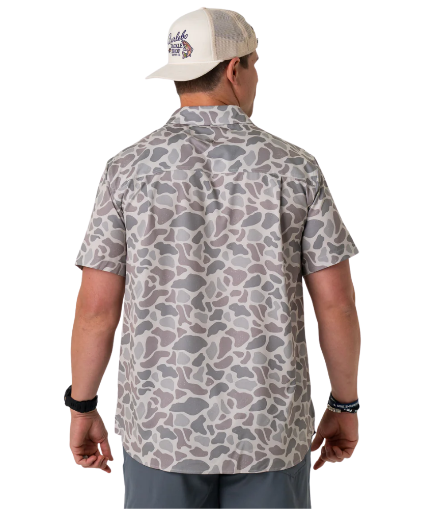 Person wearing a camouflage-patterned button-down shirt with a visible brand logo on a white background