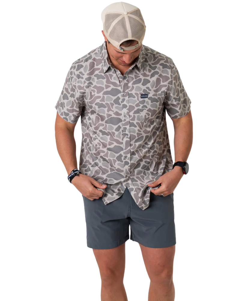 Person wearing a camouflage-patterned button-down shirt with a visible brand logo on a white background
