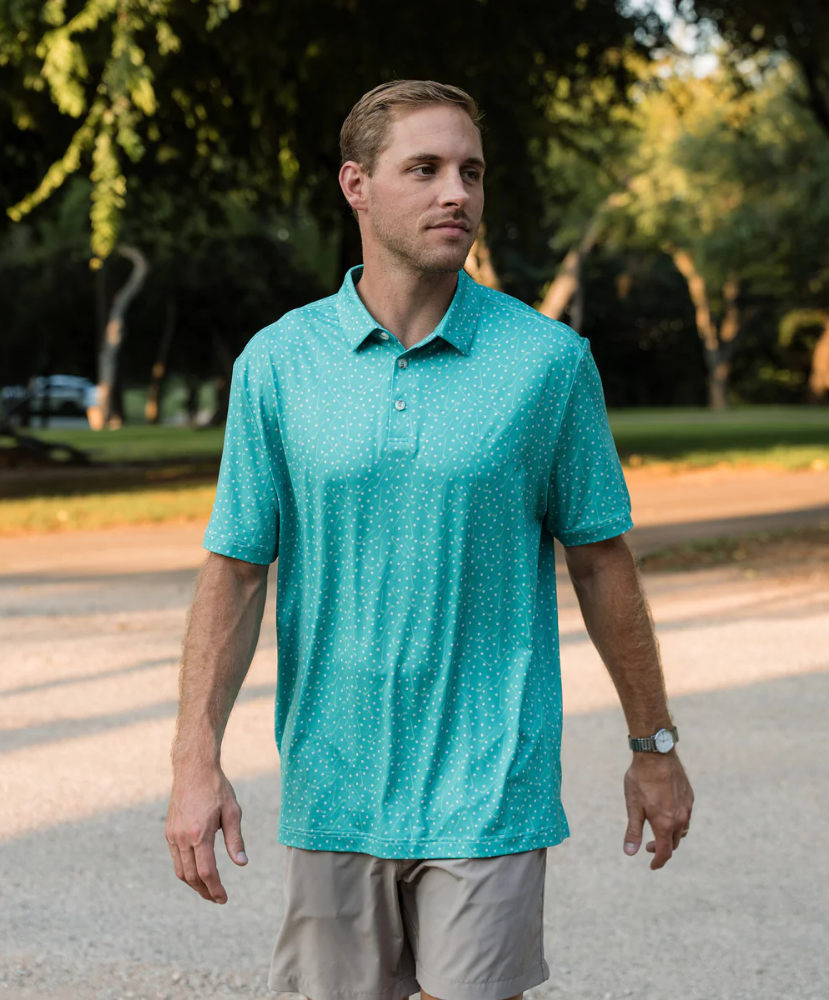 Man wearing a teal golf club and golf ball dot polo shirt on a white background