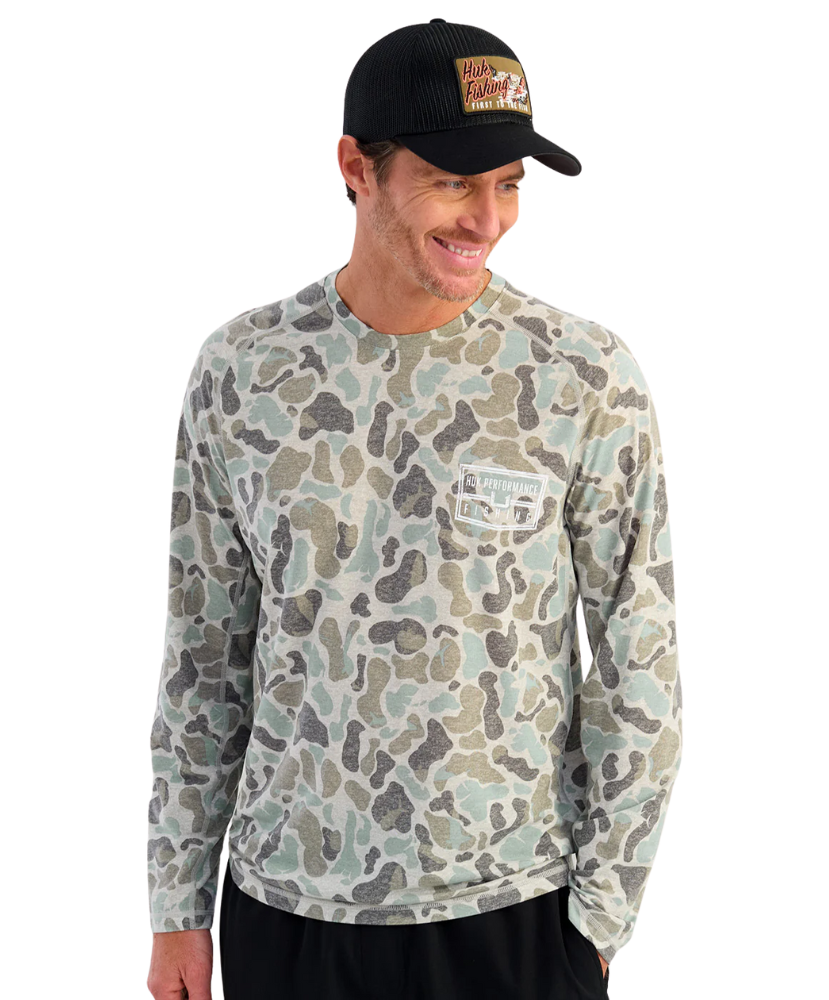 Man wearing a camouflage long-sleeve shirt with a HUK brand logo on the back, against a white background