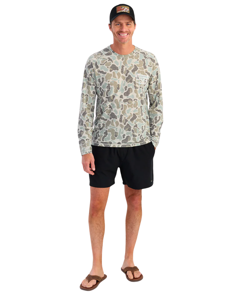 Man wearing a camouflage long-sleeve shirt and black shorts on a white background