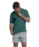 Man wearing a Green polo shirt with deer antler pattern and light gray shorts on a white background