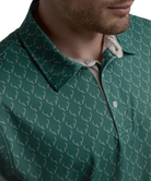 Man wearing a Green polo shirt with deer antler pattern and light gray shorts on a white background