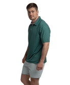 Man wearing a Green polo shirt with deer antler pattern and light gray shorts on a white background