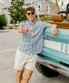 Man in a USA striped shirt and sunglasses leaning against a turquoise truck bed.