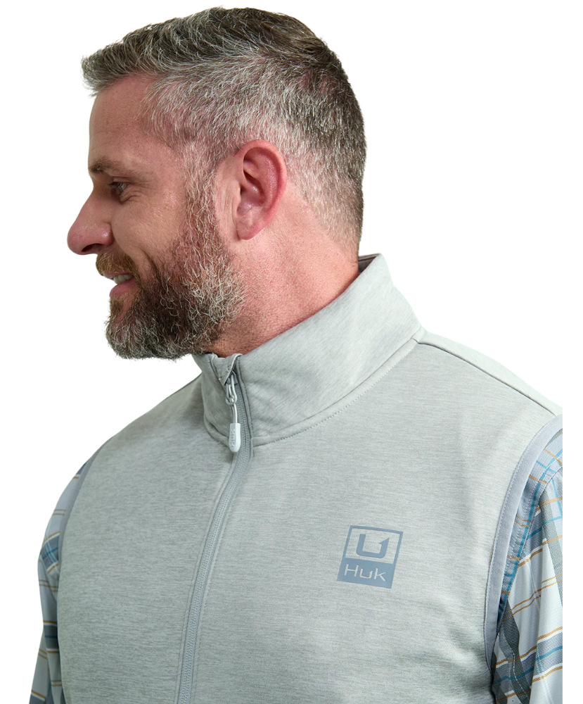 Man wearing a light gray vest WITH ZIPPER over a plaid shirt on a white background HUK GEAR
