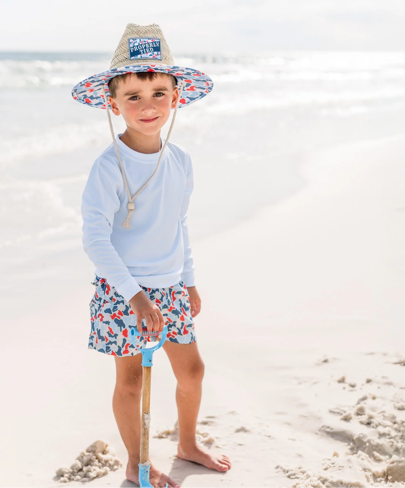 Child on a beach wearing a sun hat and colorful swim shorts.