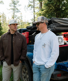 Two men standing next to a truck with an open bed in a forested area.