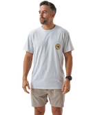 Man wearing a light gray t-shirt with a logo and beige shorts on a white background