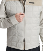 Close-up of a person wearing a beige and gray quilted jacket with a white background