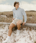Man sitting on a wooden fence in a field with a cloudy sky.