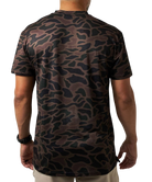 A man viewed from the back wearing a short-sleeve crewneck t-shirt with a dark brown and black organic camouflage pattern, paired with beige pants against a white background.