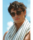 Man wearing krewe sunglasses and a striped towel against a blue sky