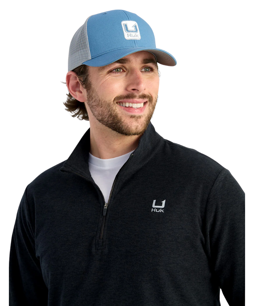 Man wearing a blue cap and black pullover with HUK logos on a white background