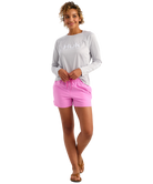 Woman wearing a gray long-sleeve shirt and pink HUK shorts on a white background
