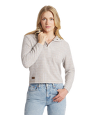 Woman wearing a light gray patterned sweater and blue jeans on a white background